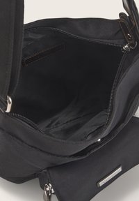 Schwarze Stofftasche mit einem Reißverschluss, ausgestattet mit einem Innenfach und einer glatten Oberfläche. Enthält ein kleines Vorderfach mit einem silbernen Akzent.