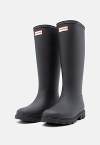 Black rubber rain boots with a smooth finish, high shaft, and a treaded sole. Features red and white "HUNTER" branding on the front.