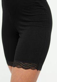 Zwarte katoen shorts met een slim fit ontwerp, voorzien van een kanten rand aan de onderkant. De textuur is glad, met een subtiele glans.