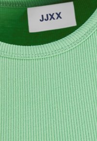 Närbild av en ljusgrön ribbad stickad tyg med en sydd halsringning och en vit etikett som visar "JJXX" i svart text.
