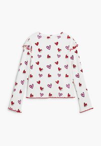 Biele rebrované tričko s dlhým rukávom s potlačou srdca v červenej a ružovej farbe, s červenými zvlnenými detailmi na výstrihu a rukávoch.