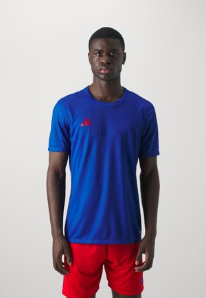 Blaues Sport-T-Shirt mit kurzen Ärmeln, Rundhalsausschnitt und rotem Adidas-Logo auf der Brust. Kombiniert mit roten Shorts. Der Stoff fühlt sich glatt und leicht an.