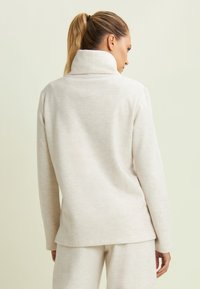 Pullover beige chiaro con colletto alto, morbida texture e maniche lunghe. Il capo presenta una vestibilità rilassata e un design semplice.