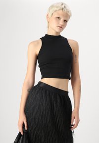 Black ribbed crop top with a high neckline. Paired with a black fringed skirt featuring a smooth waistband. Both items have a sleek texture.
