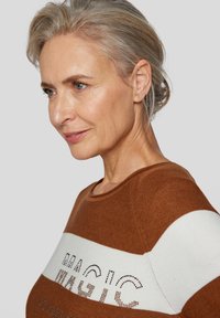 Braun-weißer Strickpullover mit runder Ausschnitt, horizontalen Streifen und dekorativem Schriftzug in kontrastierender Textur.