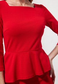 Rotes Peplum-Oberteil mit quadratischem Ausschnitt und Dreiviertelärmeln. Hergestellt aus glattem Stoff mit tailliertem Oberteil und weit ausladendem Saum.