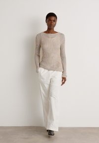 Lightly textured, beige knit sweater with long sleeves, paired with high-waisted, white wide-leg trousers and gray ankle boots.