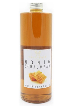 Clear bottle of amber honey foam bath liquid with a white label featuring honeycomb illustration and German text.
