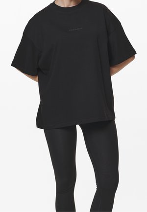 Czarny, duży t-shirt z krótkim rękawem, wykonany z miękkiej bawełny, z delikatnym logo "PEGAJOR" na środku. Połączony z czarnymi legginsami.