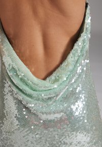 Muntgroene jurk met kraag en een reeks pailletten op een gestructureerde stof, met een gladde achterkant en reflecterende lichtdetails.