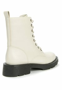 Botín de piel lisa color crema, con puntera redonda, suela gruesa negra y cierre de cordones con ojales plateados.