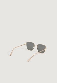 Gafas de sol con marco dorado, lentes cuadrados grises y almohadillas nasales transparentes, descansando sobre una superficie clara.