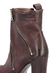 Bota de cuero marrón hasta el tobillo con cremalleras plateadas, tacón alto, parte superior texturizada y una lengua en la parte posterior para facilitar el uso.
