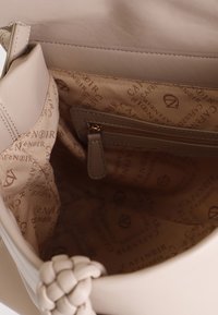 Beige læderhåndtaske indeni med en glat tekstur, der har en lynlås-lomme og et foer prydet med brandnavnet i et gentaget mønster.