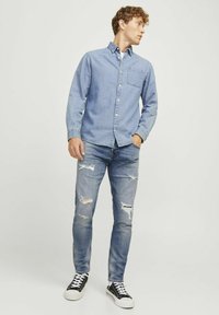 Világoskék farmering, gombos gallérral és egyetlen mellzsebből áll, amelyet elhasználódott világoskék farmernadrággal és fekete sportcipővel párosítanak.