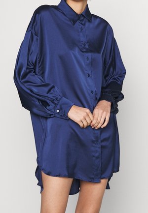 Granatowa satynowa koszula z zapięciem na guziki z przodu, długimi rękawami i marszczonymi mankietami. Posiada klasyczny kołnierzyk i zaokrąglony dół.