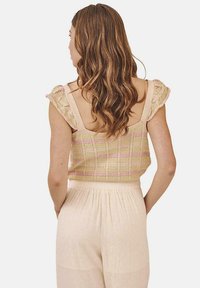 Top de punto con patrón a rayas en tonos pasteles de beige y rosa; cuenta con mangas con volantes y un diseño de espalda abierta, combinado con pantalones sueltos de color claro.