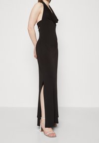 Black halter-neck gown featuring a draped neckline, side cutouts, a thigh-high slit, and a sleek, fitted silhouette.