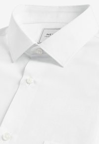 Camisa blanca de vestir con un collar clásico, dos cierres de botón y una tela suave y texturizada. La etiqueta dice "NEXT TAILORED".