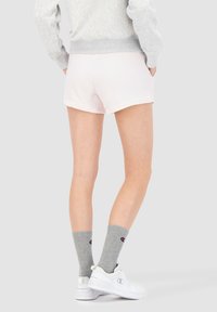 Pantalones cortos de algodón color rosa claro con un corte relajado, combinados con calcetines grises que presentan un logo, zapatillas blancas y un suéter gris.