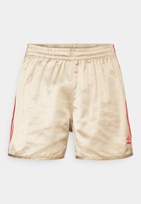 Beige träningsshorts med vertikala ränder, elastisk midja och röda sidoränder. Har en röd Adidas-logotyp i nedre vänstra hörnet.