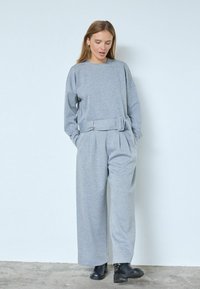 Helehall hall toonis sobiv komplekt, mis koosneb pika varrukaga üle mõõdu ülepaisutatud dressipluusist ja vööga laia säärega pükstest. Materjal tundub pehme ja tekstuuriga.