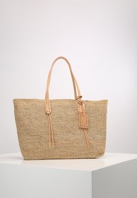 Borsa a tracolla in paglia intrecciata di colore beige con due manici in pelle robusti, caratterizzata da un'etichetta decorativa e dettagli cuciti sui lati.