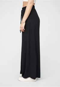 Black, elastic-waist maxi skirt made of soft fabric, featuring a loose fit and side slits. Paired with white sneakers.