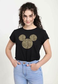 Camiseta negra con un diseño de la silueta de Mickey Mouse en estampado de leopardo. Mangas cortas. Combinada con unos vaqueros de tiro alto en azul claro.