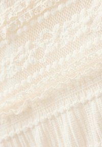 Tissu en dentelle couleur crème avec des motifs floraux et des points texturés, avec des sections froncées et volantées.