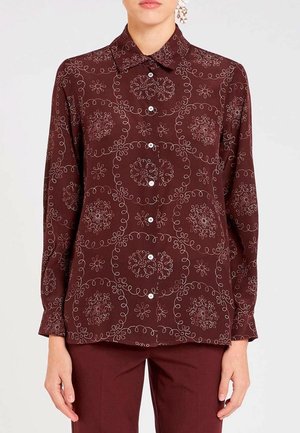 Blusa marrone a maniche lunghe con motivi floreali bianchi circolari, design con colletto e chiusura con bottoni. Tessuto morbido con una vestibilità comoda.