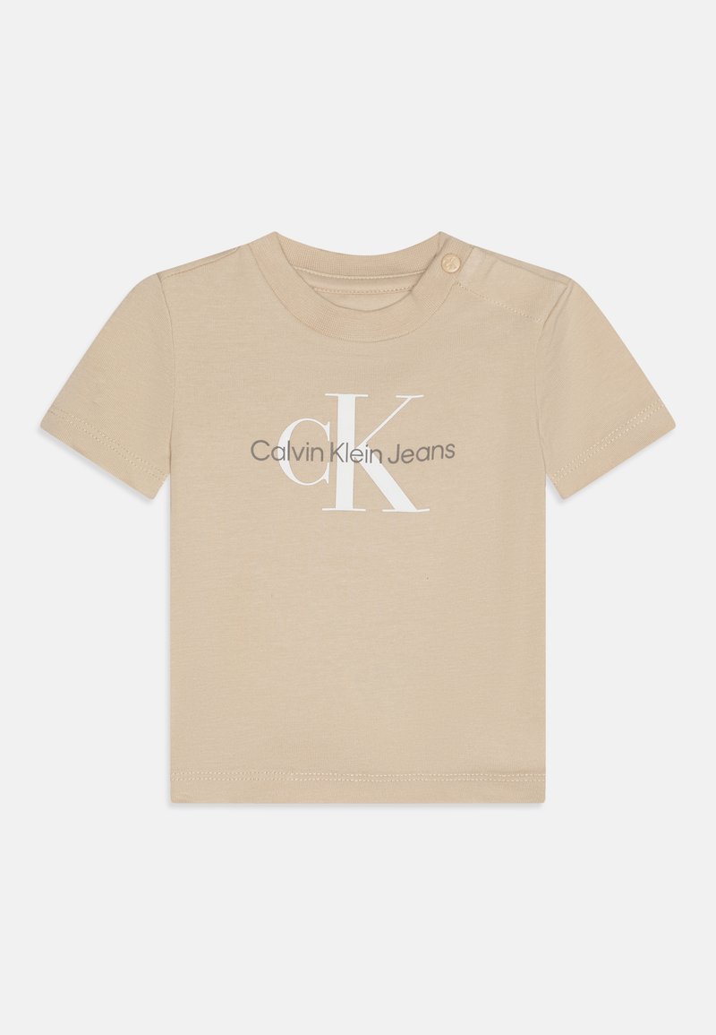 Bēša kokvilnas T-krekls ar īsām piedurknēm, kura priekšpusē ir balta CK logo un teksts "Calvin Klein Jeans". Apkaklei ir viens pogas dekors.