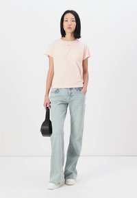 Tricou din bumbac de culoare roz deschis, cu mâneci scurte, asortat cu blugi evazați de culoare albastru deschis. Modelul ține o geantă mică de culoare neagră. Adidași albi.