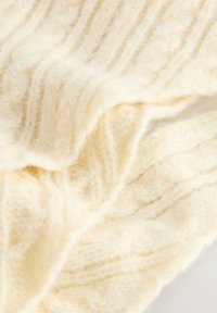 Tessuto lavorato a maglia di colore crema che mostra una consistenza morbida e soffice con motivi a treccia e a coste in primo piano.