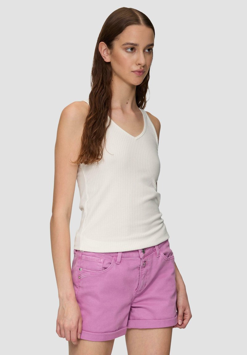 Weißes, geripptes Tanktop mit V-Ausschnitt, kombiniert mit hellrosa Shorts, die über Fronttaschen und umgeschlagenen Säumen verfügen. Model steht mit langen Haaren.
