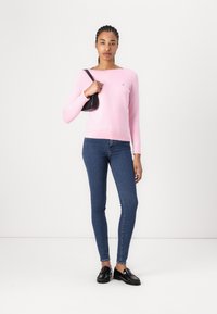 Lys rosa langermet genser med rund hals og lite logo, kombinert med mørkeblå skinny jeans og svarte loafers.