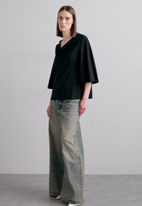 Black cowl-neck top with wide sleeves, paired with light green, straight-leg denim jeans featuring a faded finish. Set against a neutral background.