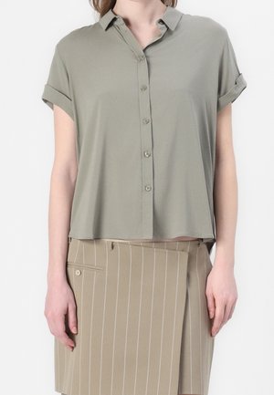 Zielona koszula na krótki rękaw z gładkiego materiału zapinana na guziki. Posiada kołnierzyk i podwinięte rękawy. Połączona z beżową spódnicą w paski.