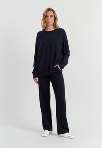 Felpa a maglia blu navy con maniche lunghe e vestibilità comoda, abbinata a pantaloni a gamba larga coordinati. Scarpe da ginnastica bianche completano l'outfit.