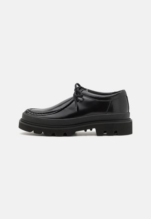 Chaussures derby en cuir noir au design élégant, bout rond et semelle en caoutchouc texturé avec des rainures profondes pour une meilleure traction.
