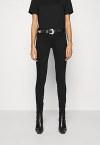 Jeans negros ajustados de cintura alta, combinados con una camiseta negra y un cinturón ancho negro con una hebilla decorativa de plata. Botines negros de tacón.