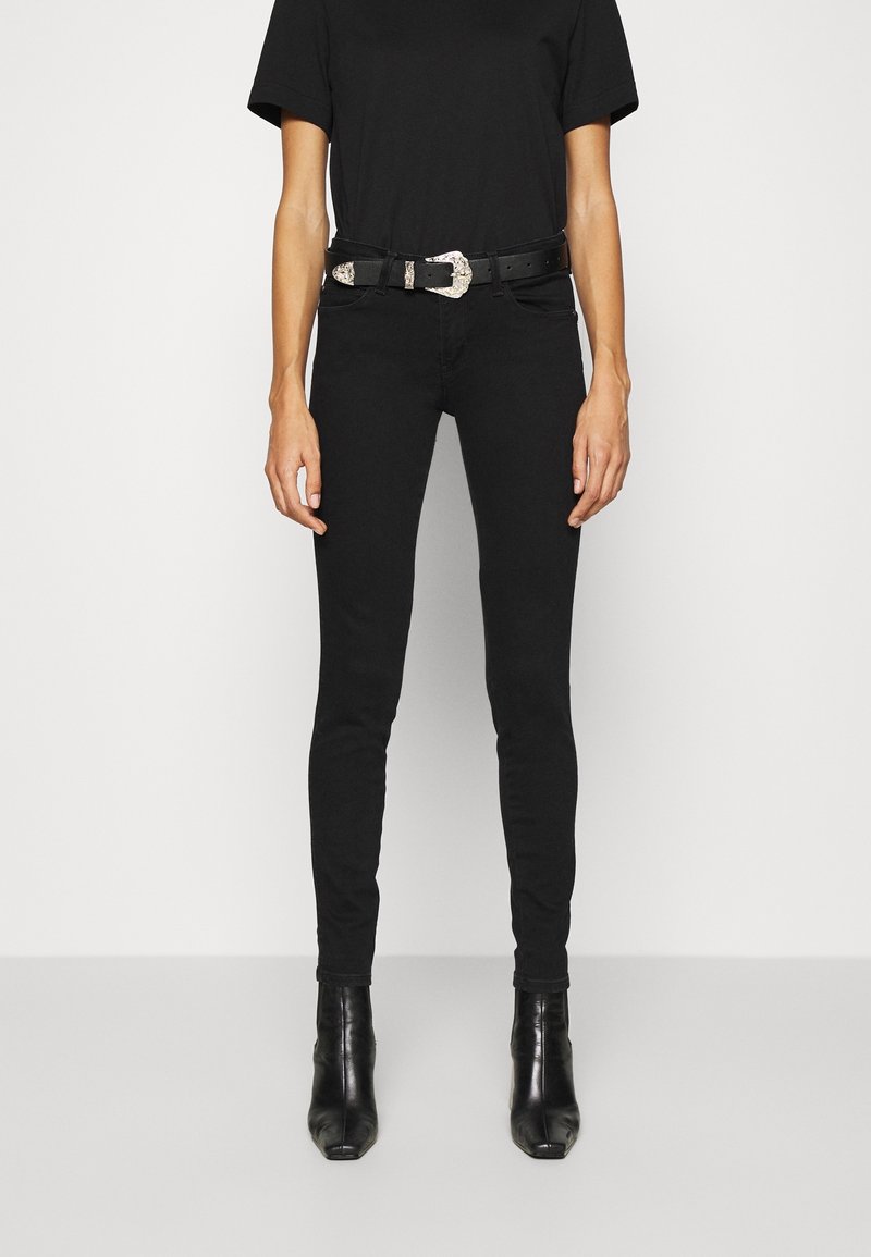 Jeans negros ajustados de cintura alta, combinados con una camiseta negra y un cinturón ancho negro con una hebilla decorativa de plata. Botines negros de tacón.