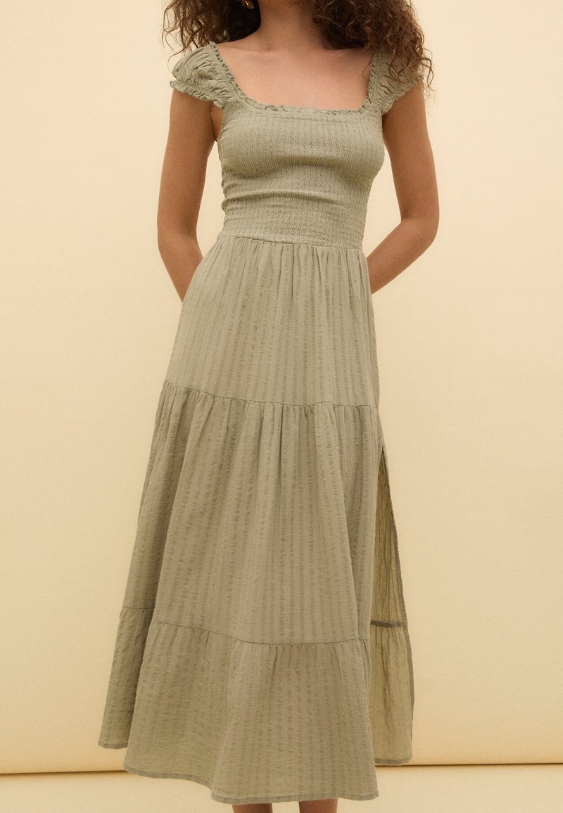 Robe midi vert clair à étages avec un décolleté carré, des manches volantées et un tissu texturé. Comprend des poches latérales et une fente sur le côté.