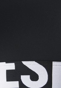 Zwarte sportstof met een contrasterende witte elastische band met grote, vetgedrukte tekst. Het oppervlak heeft een gladde, textuurachtige uitstraling.