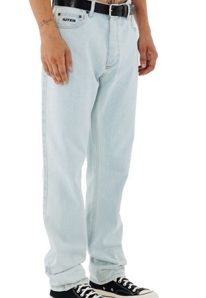 Modèle portant un jean ample bleu pâle avec une ceinture noire et des baskets en toile noires, sur fond blanc.