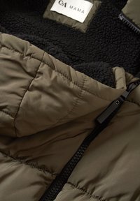 Olivengrøn vatteret jakke med sort fleecefor, der har quiltet tekstur, lynlåslukning og et mærke med teksten "C&A MAMA."