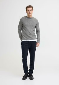 Maglione grigio lavorato a maglia con collo rotondo, abbinato a pantaloni scuri. La consistenza è morbida, con un design minimalista. Scarpe nere completano il look.