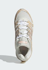 Viegls sporta apavu modelis ar baltu tīkla auduma augšdaļu zelta akcentiem, sešām baltām šnurēm un mīkstinātu iekšzoli ērtībai.