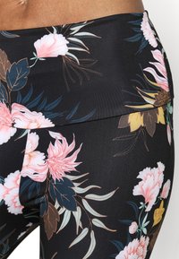 Legginsy w kwiaty wykonane z czarnego materiału, z wyrazistym różowym i żółtym wzorem kwiatowym, gładką fakturą oraz szerokim, wygodnym pasem.