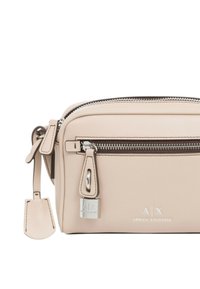 Borsa a tracolla in pelle beige con chiusura a doppia zip, hardware argentato, dettaglio con logo e tracolla regolabile. Forma rettangolare compatta.